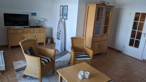 Uma sala de estar com duas cadeiras de vime, uma mesa de madeira, um armário, uma televisão e um rádio.
