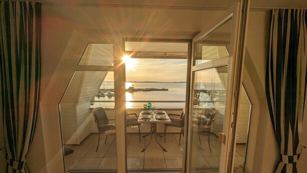 Quarto com mesa posta para dois, uma cadeira e vista para o mar através de grandes portas de vidro.