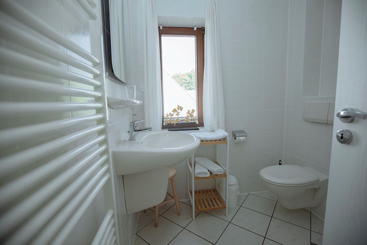 A bathroom with a white sink, a toilet, and a window with a view of greenery.
