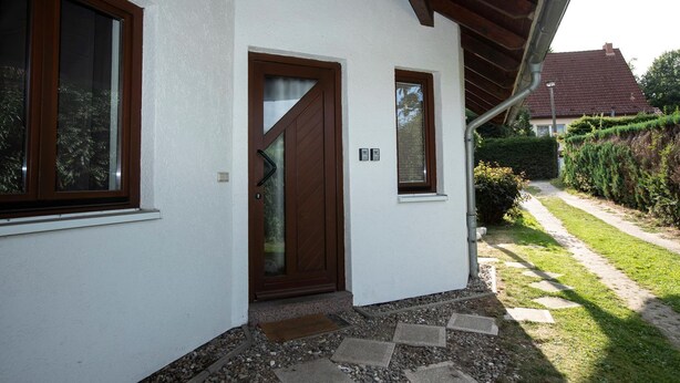 Una casa con fachada blanca, puerta marrón y una ventana pequeña.