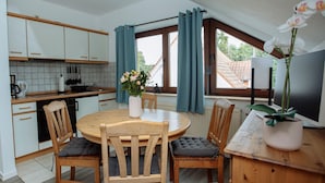 Una cocina compacta con armarios blancos, una mesa de comedor con cuatro sillas y una orquídea en maceta.