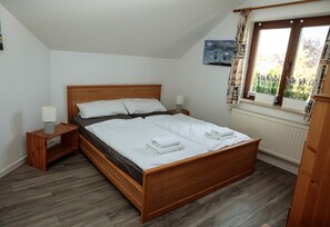 A bedroom with a wooden bed, two bedside tables, a window with curtains, and a radiator. - Milana Apartment - Perfect for Two, Parking - Milana Apartment - Sun, (Putbus)