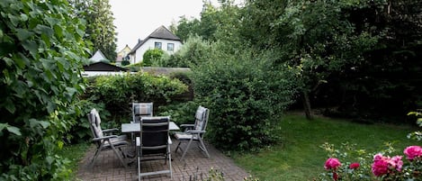 A patio area with a table and chairs, surrounded by lush greenery and flowering plants.