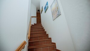 Una escalera con barandillas de madera y piso de baldosas, que lleva a un rellano con una puerta.