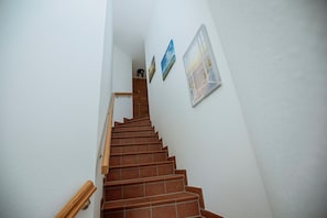 Eine Treppe mit hölzernen Geländern und Fliesenboden, die zu einem Zwischenpodest mit einer Tür führt.