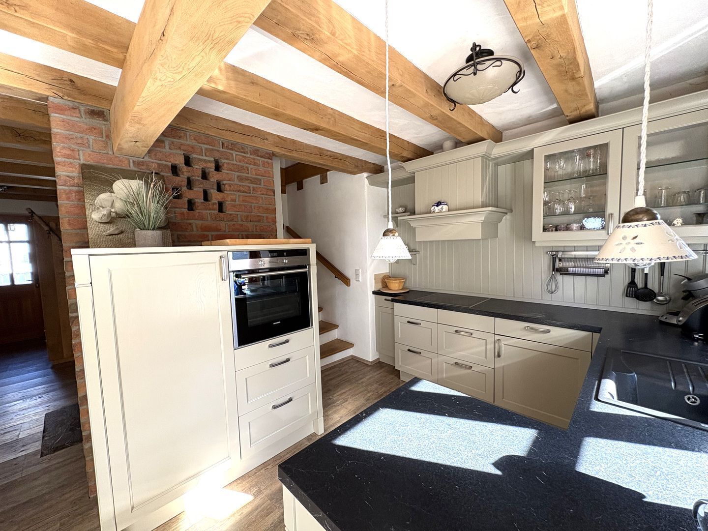 Una cucina con forno integrato, mobili bianchi, un piano di lavoro nero e travi a vista in legno.