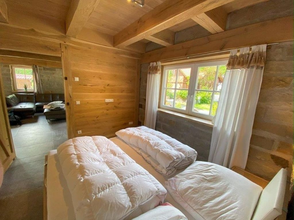 Una cabaña de madera con dos camas, una ventana con cortinas y vistas al follaje.