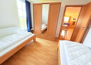 Ein Zimmer mit zwei Betten, einem Schrank, einem Spiegel und Blick auf ein weiteres Zimmer.
