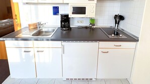 Pieni, käytännöllinen keittiö, jossa on valkoiset kaapit, mikroaaltouuni, kahvinkeitin ja pesuallas.