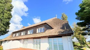 Ett traditionellt hus med ett halmtak, vitmålade ytterväggar och stora fönster.