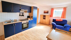 A compact kitchen with a sink, stove, and cabinets, a dining table, and a blue sofa. - Apartment Seelenfrieden 3 - with balcony for 4 persons - Cozy vacation apartment with balcony (Alt Reddevitz)
