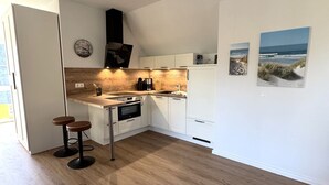 A modern kitchen with white cabinets, a wooden countertop, and a built-in oven. There are two stools and a clock on the wall. - Vacation apartment Kajüte 2 - close to the harbor, with balcony - Fully equipped (Poseritz)