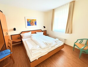 A hotel room with a single bed, a wooden chair, a small table, and a window with curtains. - Boddenhof Apartment 48 - Terrace for Dog Lovers - Apartment 48 - (Bergen)