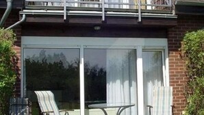 A balcony with two chairs and a table, a sliding glass door, and a brick wall. - Boddenhof Apartment 48 - Terrace for dog lovers - Holiday apartment 48 - (Bergen)