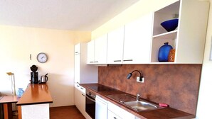 A compact kitchen with white cabinets, a stainless steel sink, a coffee maker, and a clock on the wall. - Boddenhof Apartment 48 - Terrace for dog lovers - Holiday apartment 48 - (Bergen)