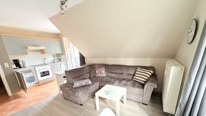 Ett kompakt bostadsutrymme med ett litet kök, en grå soffa, ett litet bord och ett element.