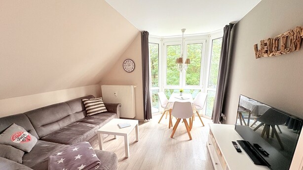 Ett modernt vardagsrum med en soffa, ett litet bord, en tv och en matplats med ett bord och stolar.