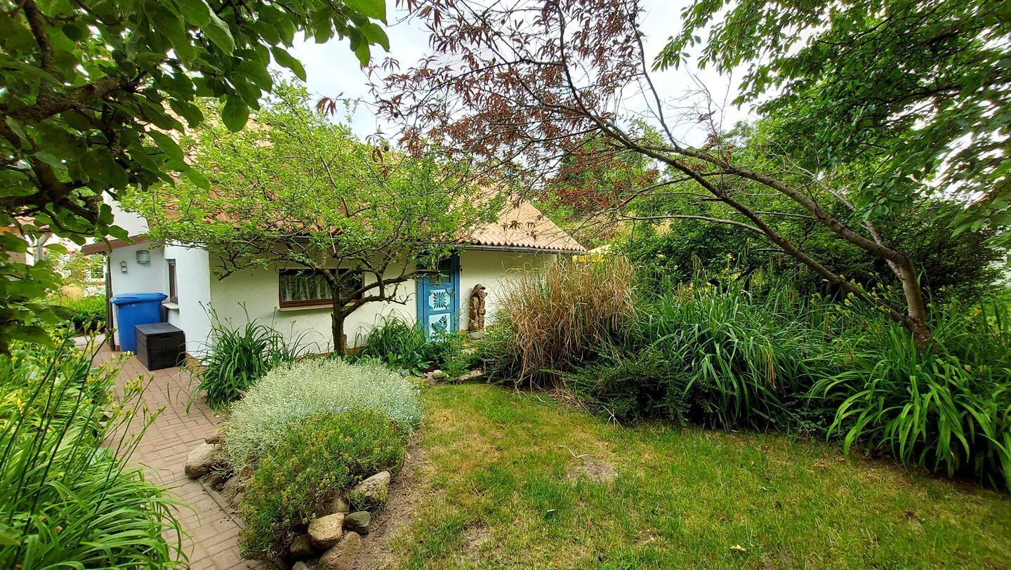 Ein kleines Haus mit Ziegeldach, umgeben von üppigem Grün und einem gepflasterten Weg.
