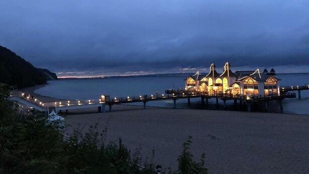Ein Küstenhotel mit einer Steg, der ins Meer hinausführt, mit mehreren Gebäuden und beleuchteten Fassaden.