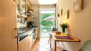 Eine kompakte Küche mit Holzausbau, einem Esstisch mit Blumenvase und Blick ins Grüne durch das Fenster.