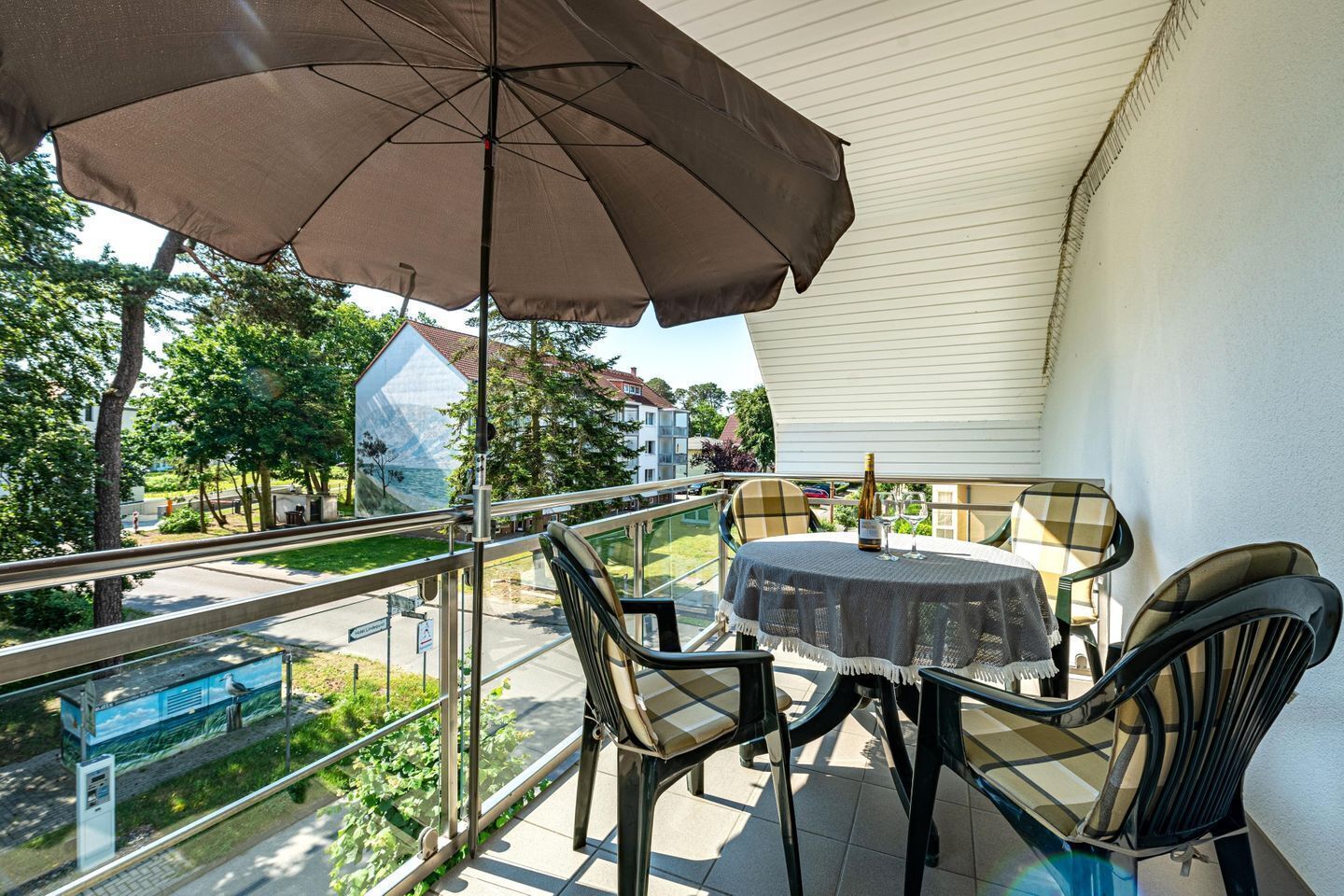 Un balcón con mesa y sillas, un toldo grande y vistas a un parque y edificios.