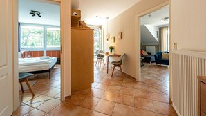 Ein geräumiger Flur mit Bett, Schreibtisch und Stuhl im Vordergrund, der in einen Wohnbereich mit Sofa und Heizkörper führt.