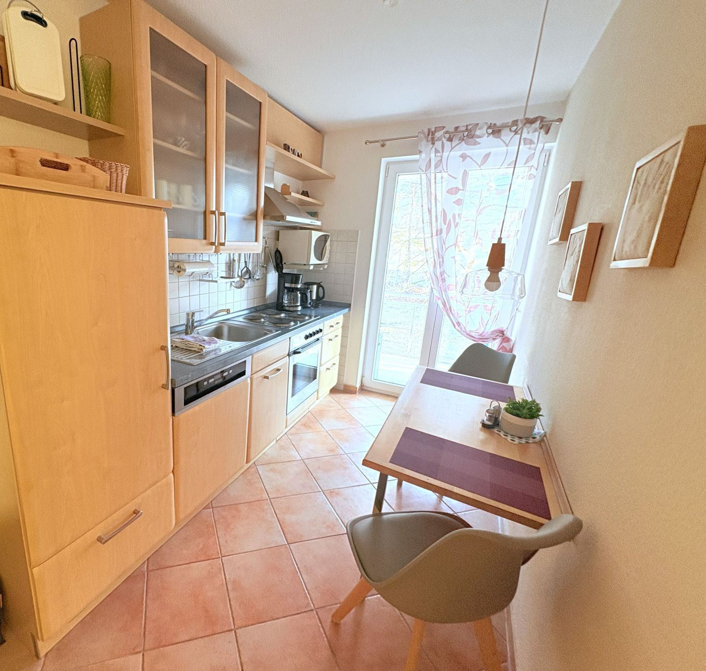 A compact kitchen with wooden cabinets, a built-in microwave, and a dining area with a table and chairs.