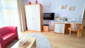 Ett vardagsrum med en röd soffa, ett skrivbord i trä med en stol, en tv och en stor garderob.