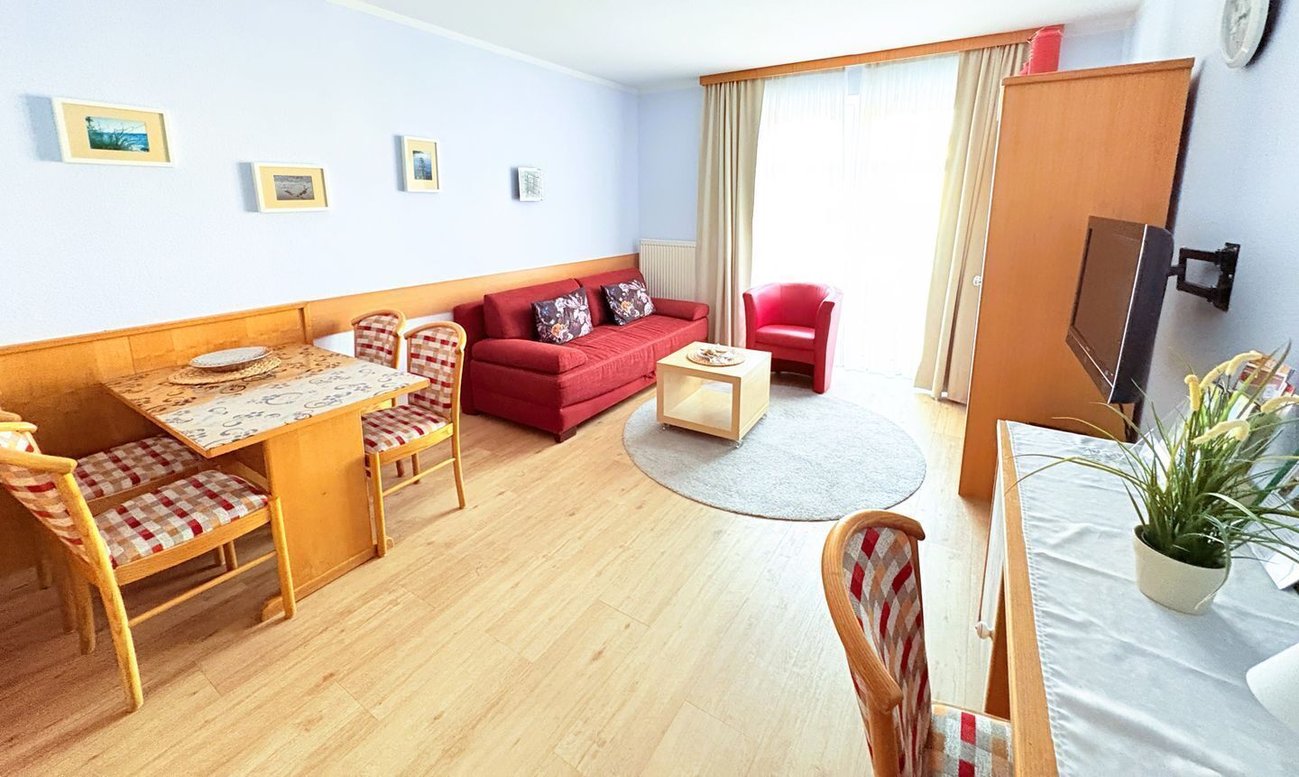 Habitación de hotel con una mesa de comedor de madera, sofá rojo y televisor en la pared.