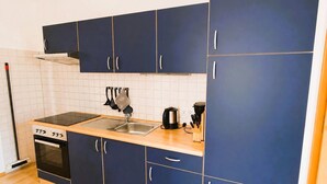 A compact kitchen with dark blue cabinets, a stainless steel sink, a stove, and a kettle. - Fewo Seelenfrieden 6 - top for 2 persons and dog - vacation apartment in Alt (Alt Reddevitz)