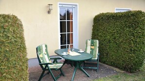 An outdoor patio with a table and two chairs, a bottle, and a glass on the table. - Fewo Seelenfrieden 6 - top for 2 persons and dog - vacation apartment in Alt (Alt Reddevitz)