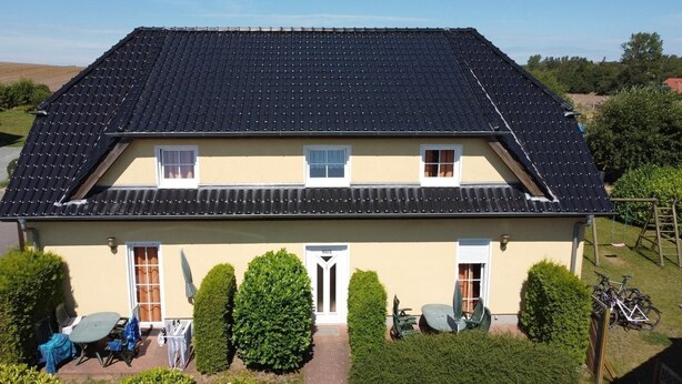 A two-story house with a tiled roof, a front door, and a small porch with outdoor seating. - Fewo Seelenfrieden 6 - top for 2 persons and dog - vacation apartment in Alt (Alt Reddevitz)