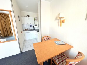 A compact kitchen with white cabinets, a microwave, and a sink. There's a wooden table with a chair, a lamp on the wall, and a checkered cushion on the chair. - Apartment 1 in Haus Hühnergott - close to the beach, ideal for Zeei - vacation apartment (Sellin)