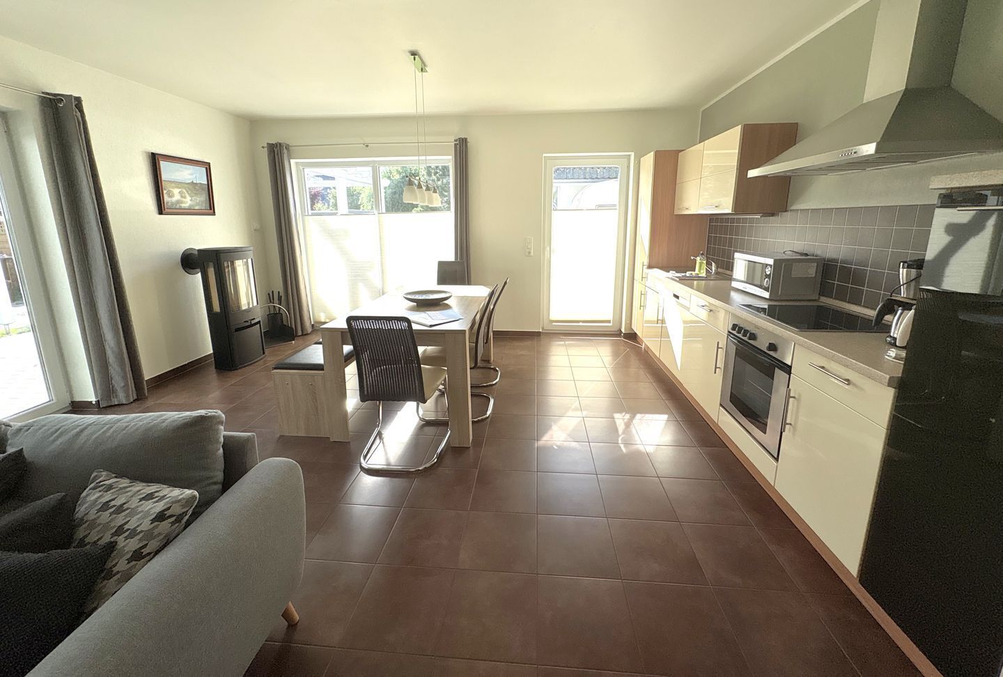 A modern kitchen with a dining area, a sofa, and a view of the outdoors.