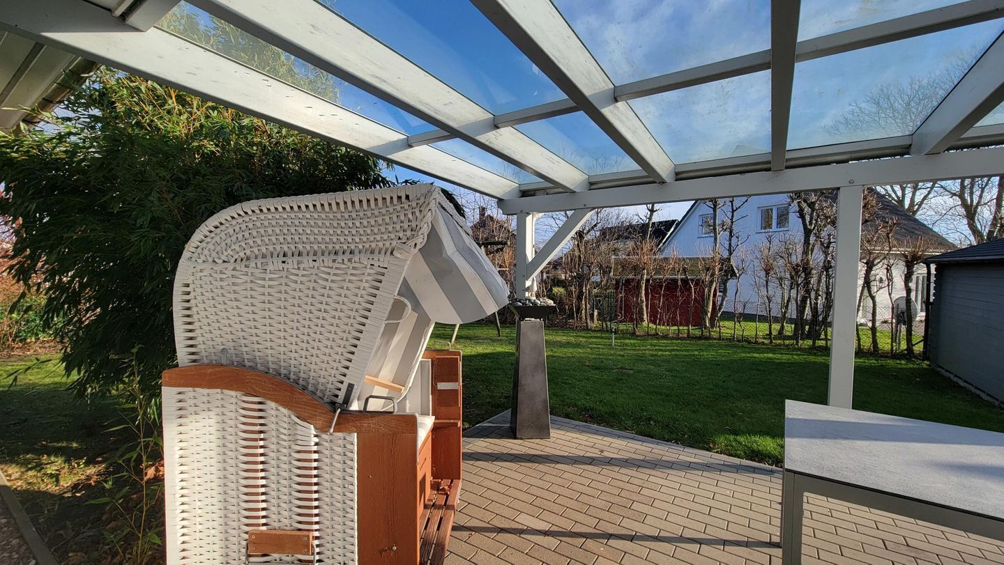 Un espace extérieur abrité, doté d’une pergola, d’un fauteuil en osier et d’un chemin en briques.