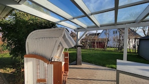 Uma área externa coberta com pérgola, uma cadeira de vime e um caminho de tijolos.