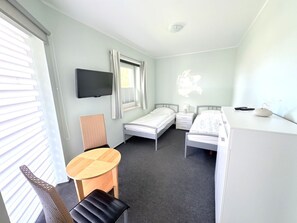 Et hotelværelse med to senge, et fjernsyn, et skrivebord, en stol og et vindue med gardiner.