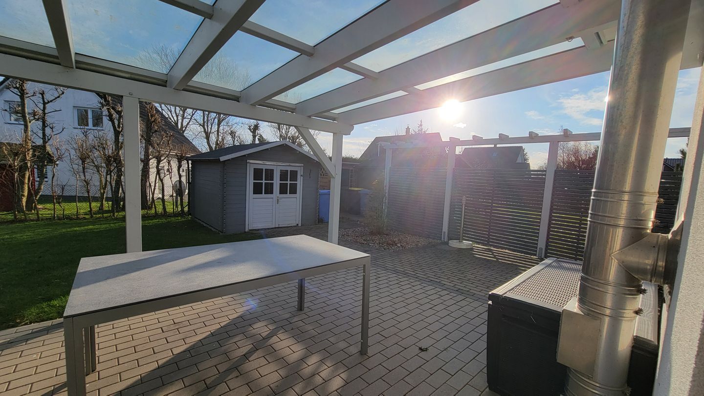 Un patio techado con una mesa, un cobertizo pequeño y una verja de metal.
