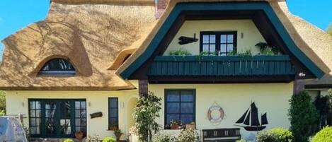 A traditional house with a thatched roof, a small garden with rocks and plants, and a sailboat mural on the wall.