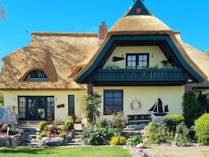 A traditional house with a thatched roof, a small garden with rocks and plants, and a sailboat mural on the wall. - Apartment 2 in the Zeesboothaus - Terrace, water view - Apartment 2 in the Zeesboothaus (Middelhagen)
