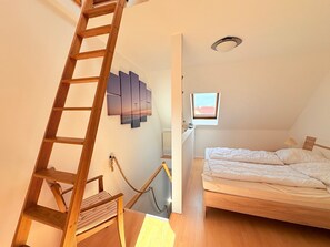 Ein Schlafzimmer mit einer Holzleiter, einem Bett, einem Fenster und einem an der Wand befestigten Kunstwerk.