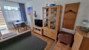 Ein Wohnzimmer mit Fernseher, Holzschrank und Essbereich mit Stühlen.
