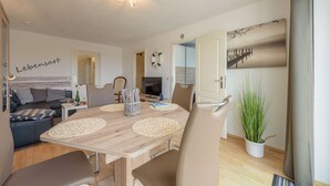 Una sala de estar moderna con una mesa de comedor de madera, sillas color beige, un sofá y un televisor.