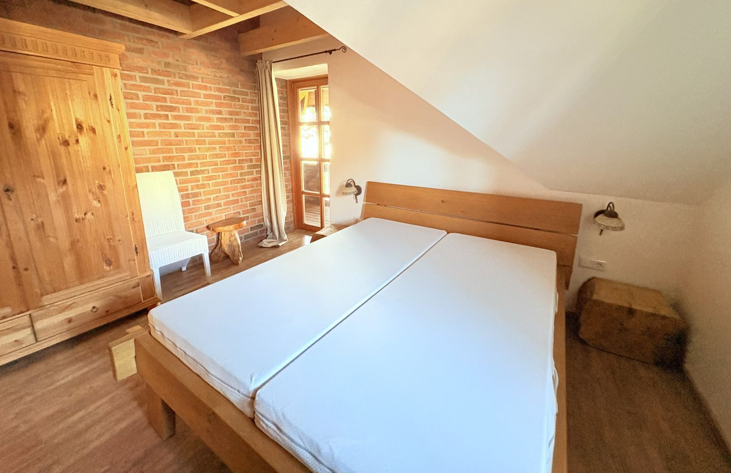 Un dormitorio con una cama de madera, una pared de ladrillo y una ventana con cortinas.