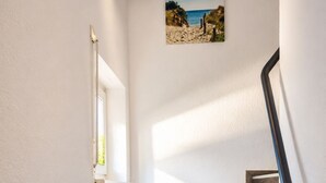 A staircase with wooden steps and a black handrail, leading to a landing with a picture of a beach scene. - Vacation home zum Kranichblick - for families + dog - Zum Kranichblick: Relaxing (Garz OT Losentitz)