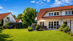 A residential property with a well-maintained lawn, a patio with outdoor furniture, and a large tree in the background. - Vacation home zum Kranichblick - for families + dog - Zum Kranichblick: Relaxing (Garz OT Losentitz)