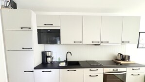 Eine moderne Küche mit weißen Schränken, einer schwarzen Arbeitsplatte, einer Kaffeemaschine, einem Wasserkocher und einem eingebauten Backofen.