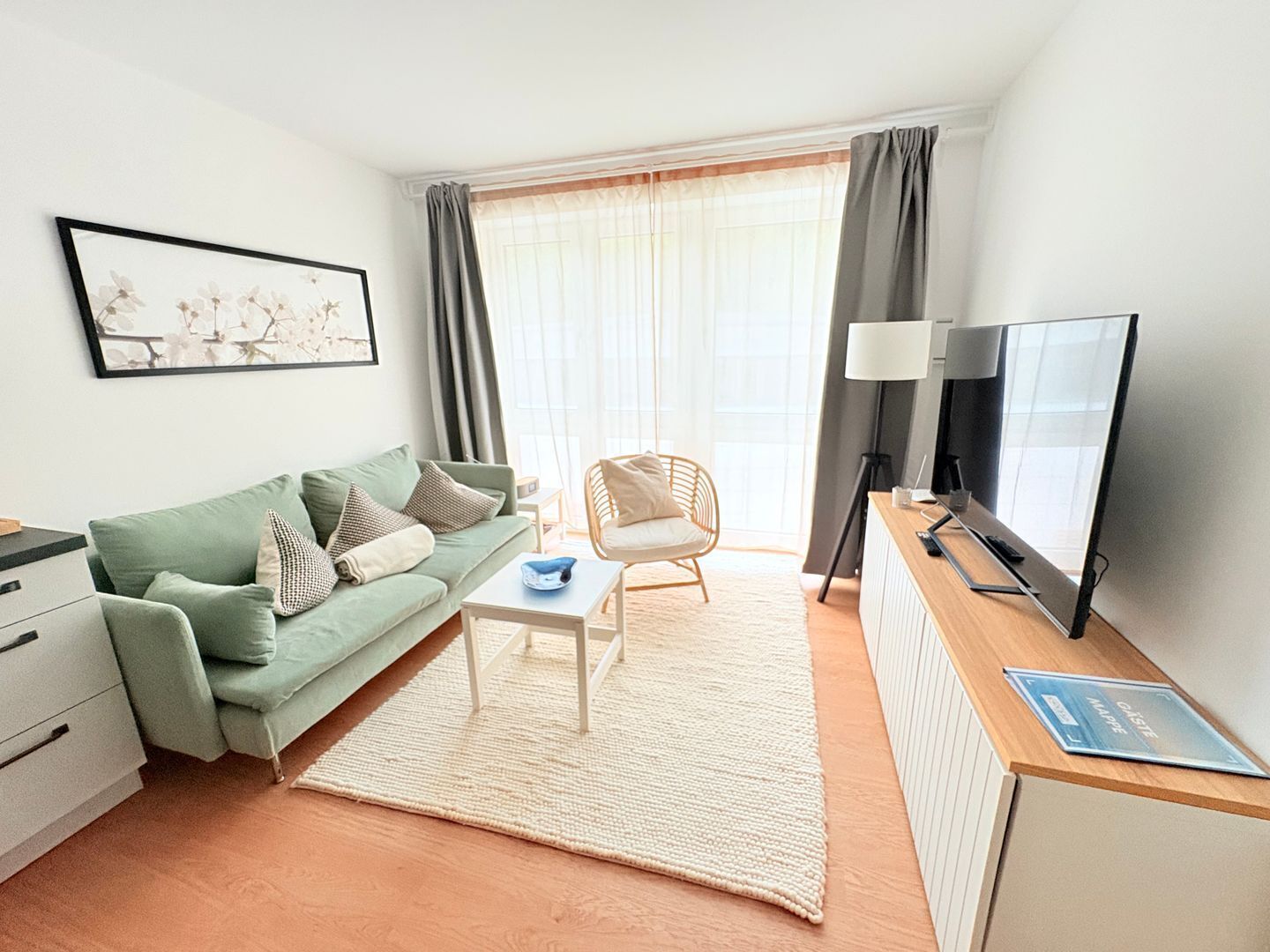En moderne stue med en grøn sofa, et hvidt sofabord, en fletstol, et fjernsyn og en radiator.