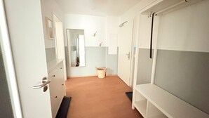 Ein schmaler Korridor mit Holzboden, weißen Wänden und einem Spiegel links.