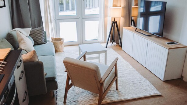 Ein modernes Wohnzimmer mit einer Couch, einem Holzstuhl, einem Fernseher auf einem Schrank und einer Lampe.